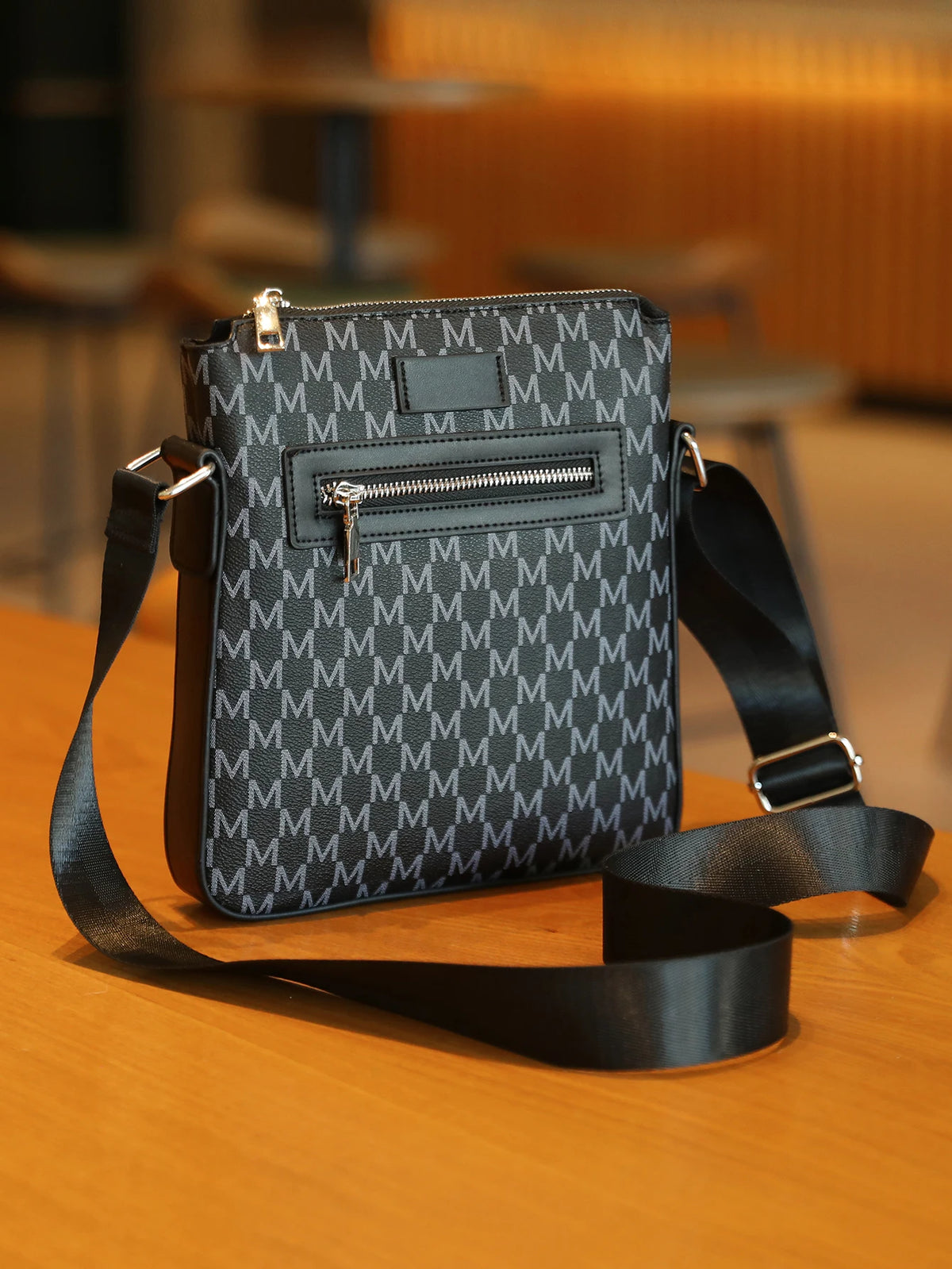 A black men's lightweight crossbody sling bag with a textured pattern resting on a wooden surface.