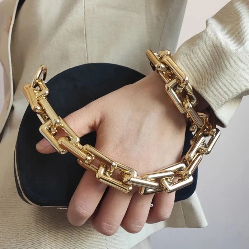 Una mano sostiene una correa de bolso de acrílico de color dorado contra un blazer beige claro.