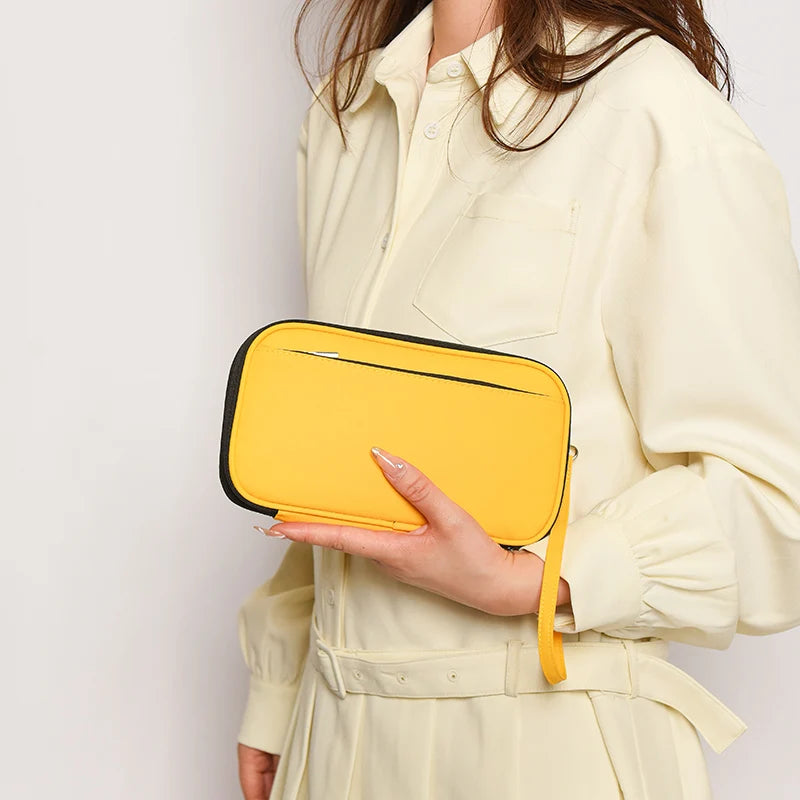 A hand holds a yellow passport organizer against a light cream-colored shirt.