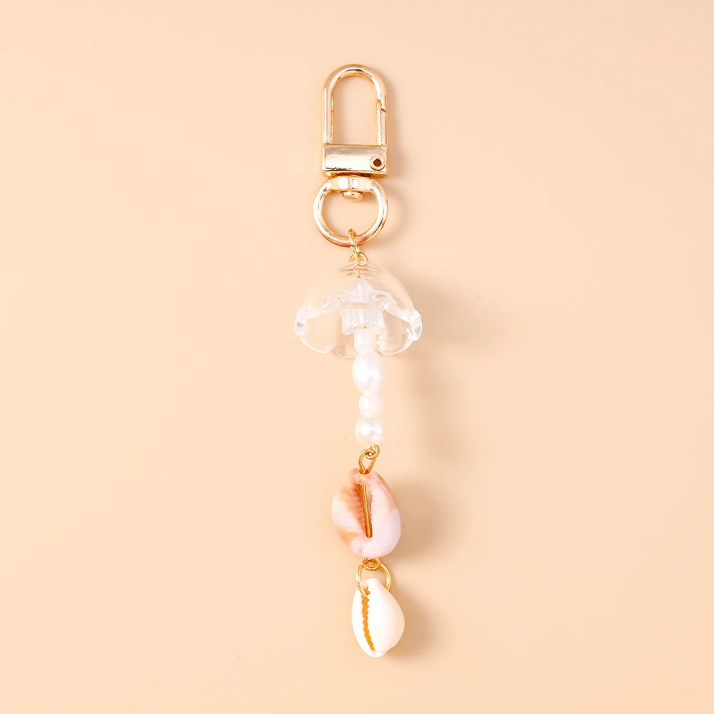 Gold-toned starfish keychain featuring a clear glass charm and a pink seashell pendant with pearl accents