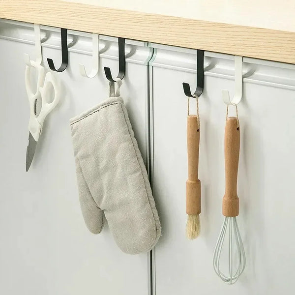 A heavy duty multi-purpose hook rack displaying kitchen tools like scissors and a whisk hanging on a cabinet door.