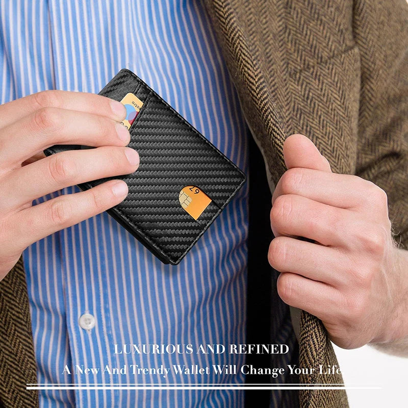 A hand holds a black slim leather wallet with a gold tag against a blue striped shirt and brown jacket.
