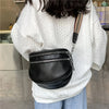 A black soft leather crossbody bag with double zippers and an adjustable strap is shown being held by a person wearing a whit