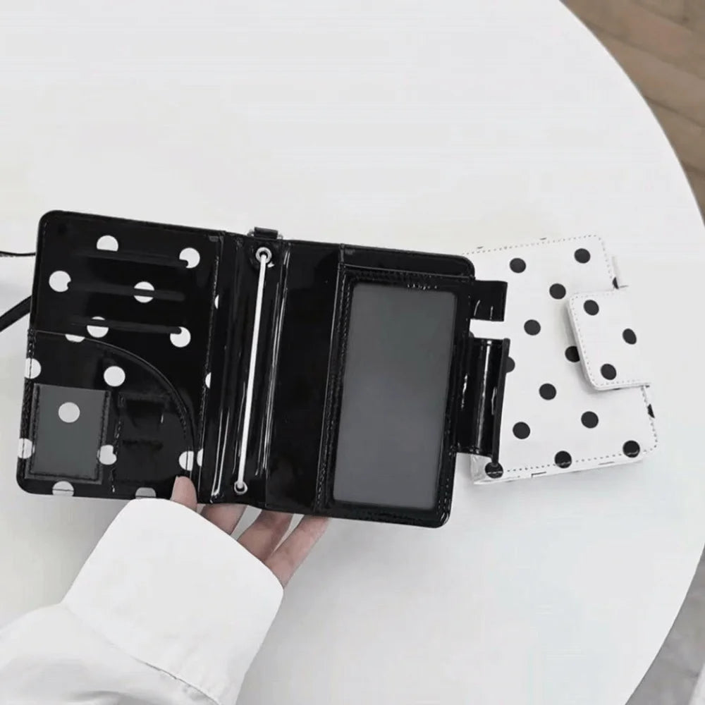 Black and white polka dot passport holder with multiple card slots resting on a white table.
