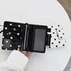Black and white polka dot passport holder with multiple card slots resting on a white table.