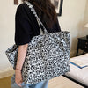 A person holds a black and white leopard print canvas tote bag with a white and gray pattern.