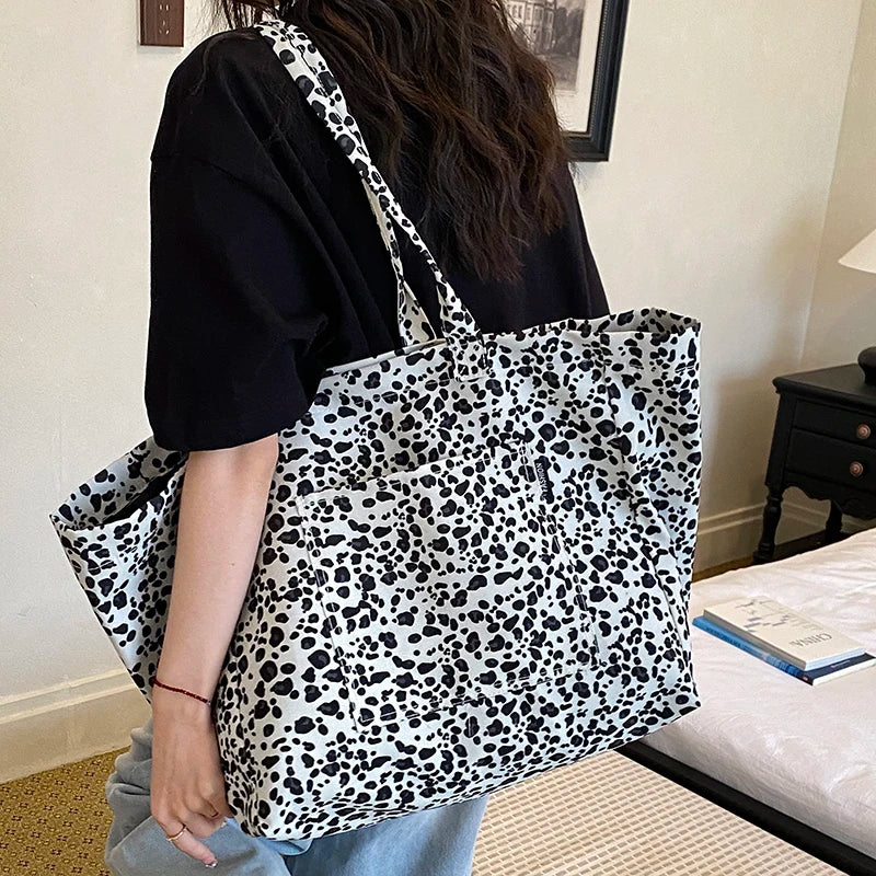 A person holds a black and white leopard print canvas tote bag with a white and gray pattern.