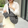 Eine Frau in weißem Hemd und hellem Rock hält eine schwarze Leinensack-Crossbodytasche mit Zebraprint.
