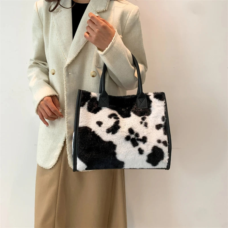 A woman holds a black and white leopard print faux fur designer shoulder tote bag in front of her.