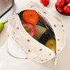 A light beige corduroy lunch bag is open, revealing fresh fruits like an orange, apple, grapes, and a yellow fruit.