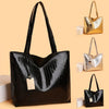 A black crocodile-textured leather tote bag with gold hardware displayed against a beige background.