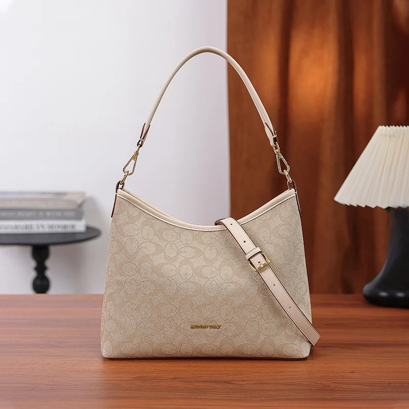 A beige leather tote bag with a letter print and bow accent resting on a wooden table.
