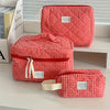 A red and white plaid cosmetic storage bag is displayed on a white shelf.