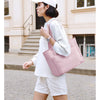 Une femme portant un chapeau et un haut blanc marche en portant un sac fourre-tout rose matelassé.