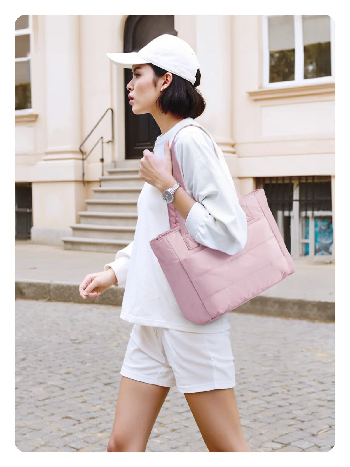 Une femme portant un chapeau et un haut blanc marche en portant un sac fourre-tout rose matelassé.