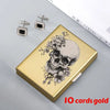 A gold card holder featuring a detailed skull design, with two silver earrings displayed nearby.