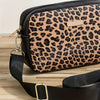 A black leopard print crossbody bag with a gold hardware strap resting on a wooden surface.
