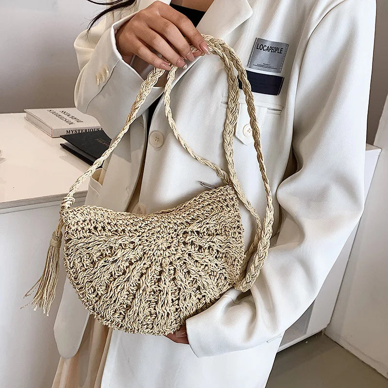 A woman holds a beige handmade rattan straw crossbody bag against a white blazer.