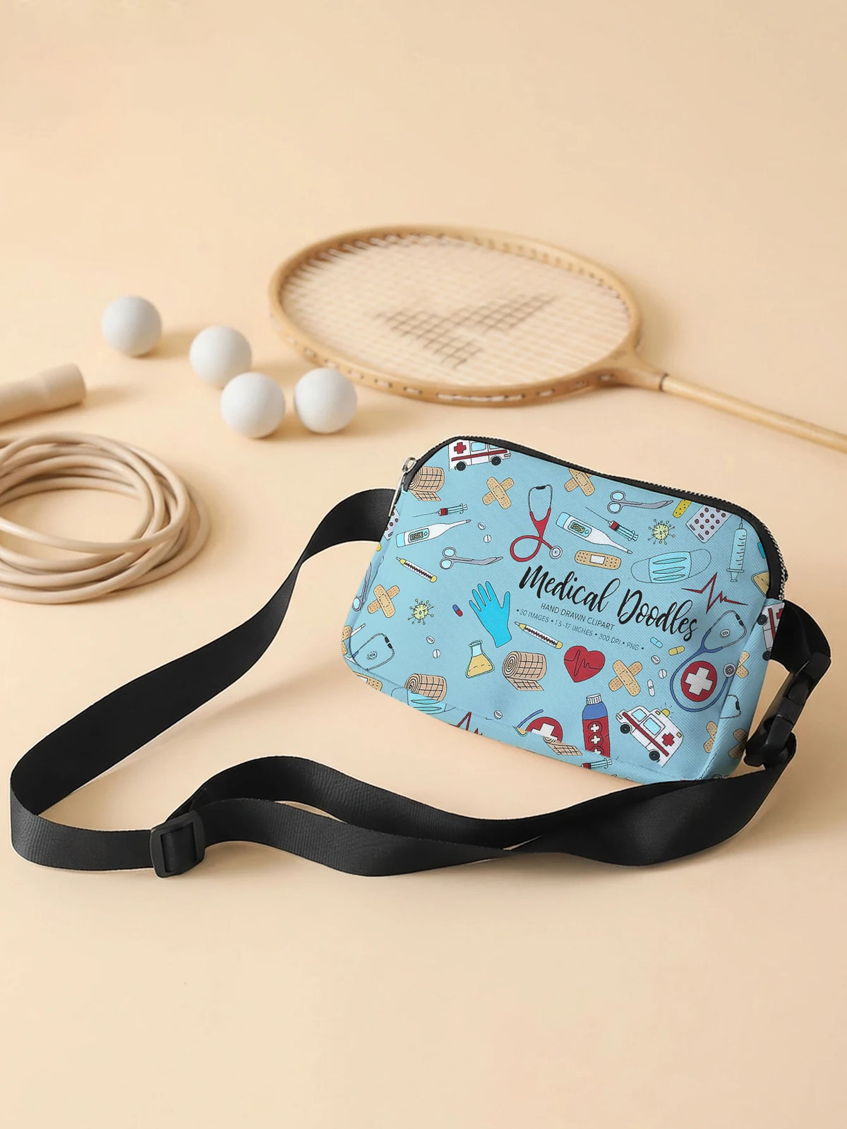 A blue medical doodle print crossbody waist bag resting on a light beige surface with a tennis racket and balls nearby.