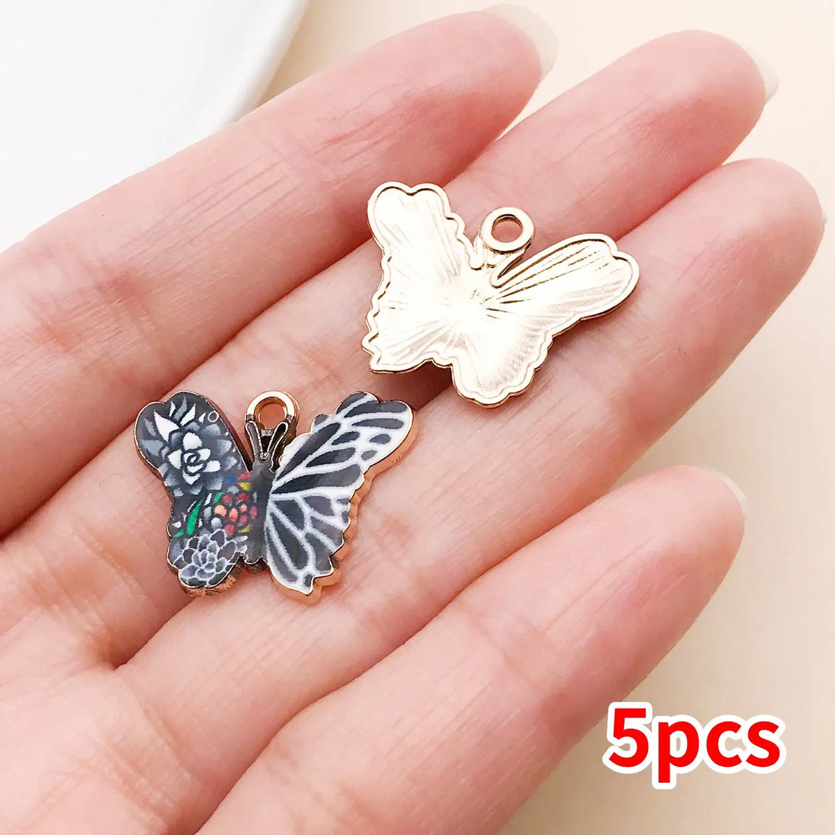A set of five colorful butterfly enamel charms displayed on a person's hand.