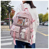 A woman wearing a white sweater carries a pink Korean style backpack with various compartments and charms on a sidewalk.