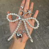 A hand holds a silver pearl bowknot keychain featuring a starfish charm and a heart pendant.