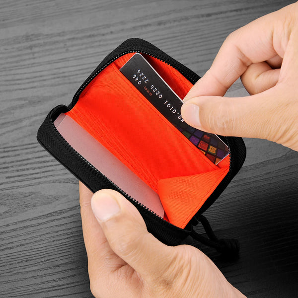 A hand is opening a black RFID zipper wallet to reveal an orange interior and a credit card.