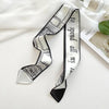 Foulard de soie rayé noir et blanc noué en nœud, exposé sur un tissu blanc.