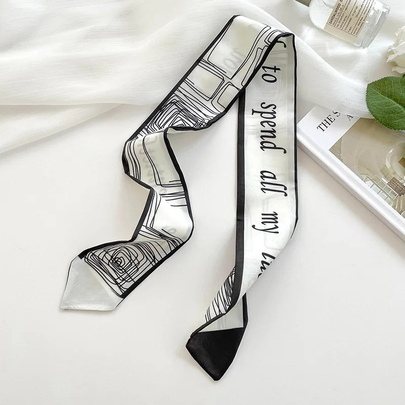 Foulard de soie rayé noir et blanc noué en nœud, exposé sur un tissu blanc.