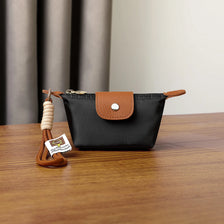A black leather coin purse with a brown flap and a woven wrist strap resting on a wooden surface.