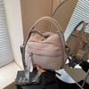 A light gray nylon crossbody bag with a top handle is displayed on a table next to a mirror.