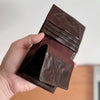 A hand holds a dark brown genuine leather bifold wallet open, showing the interior.