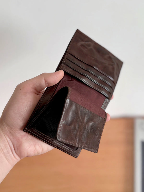 A hand holds a dark brown genuine leather bifold wallet open, showing the interior.