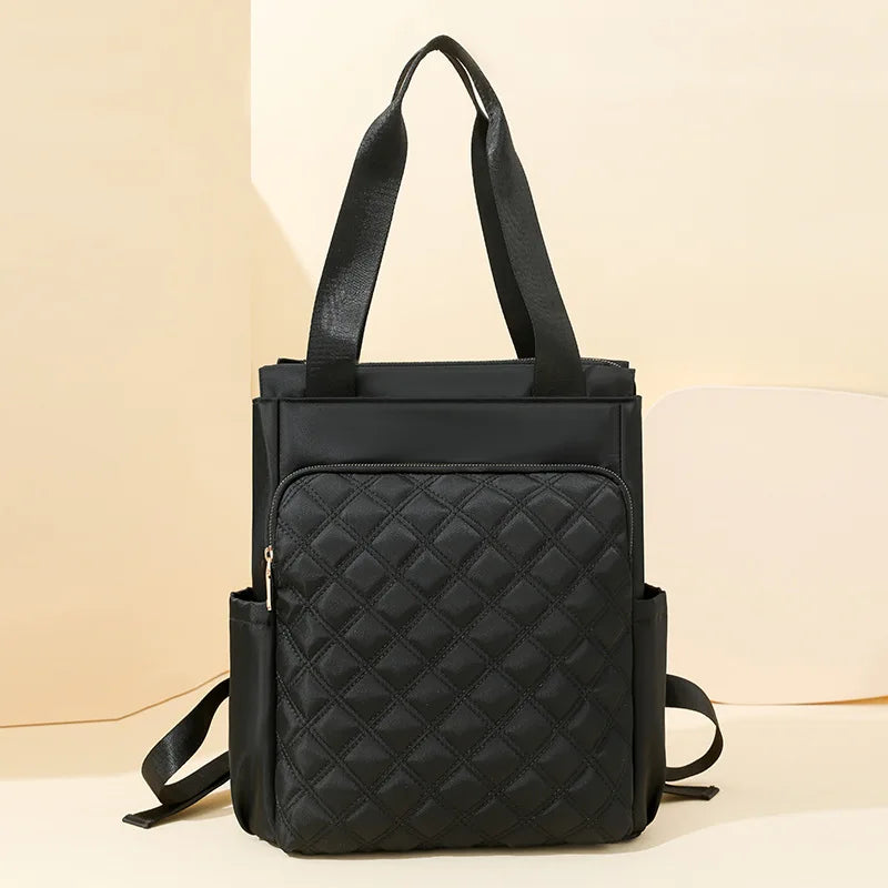 A black quilted women's backpack tote bag with black straps resting on a light background.