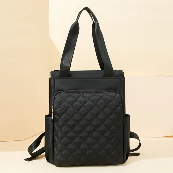 A black quilted women's backpack tote bag with black straps resting on a light background.