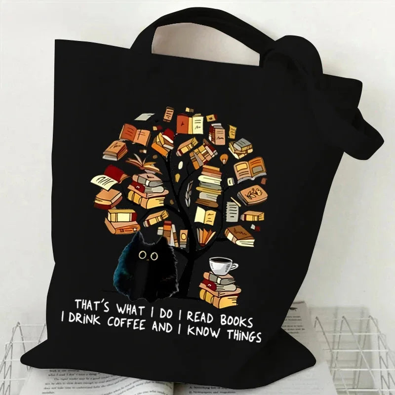 Black canvas tote bag featuring a tree made of books with a cat silhouette and butterfly details.
