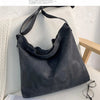 A dark gray canvas tote bag featuring a large letter design, displayed on a white surface.