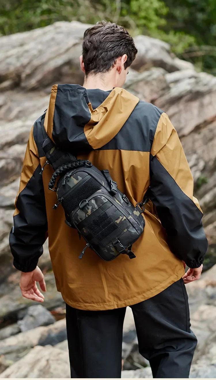 A man wearing a tan and black jacket is carrying a tactical chest bag on his back in an outdoor setting.
