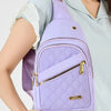 Un sac bandoulière à motif matelassé violet avec une fermeture éclair dorée porté par une personne en chemise bleu clair.