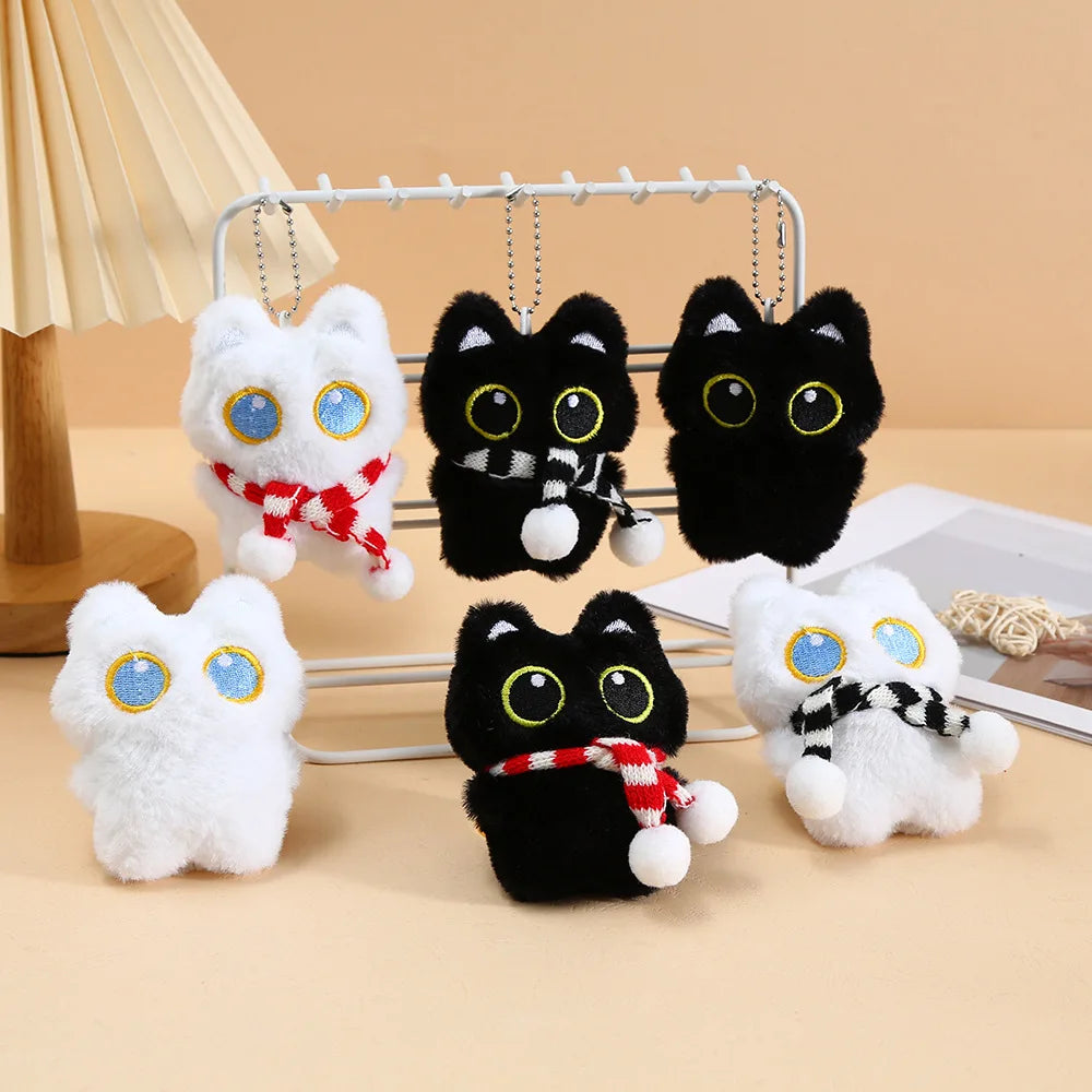A collection of cute plush black cat keychain charms with white fur and red accents displayed on a metal rack.