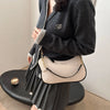 A woman holds a beige crescent crossbody bag with gold hardware and a gray pleated skirt.