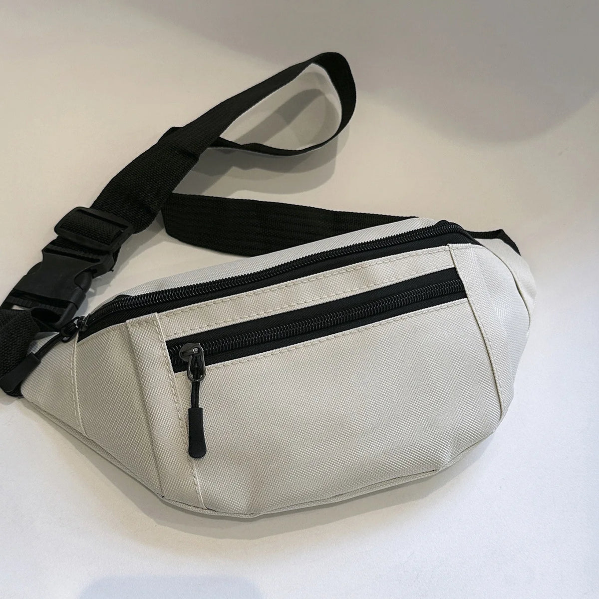 A light beige compact nylon waist bag with black straps and a zippered compartment.