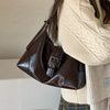 A brown retro PU leather underarm bag carried by a woman wearing a cream knit sweater and plaid skirt.