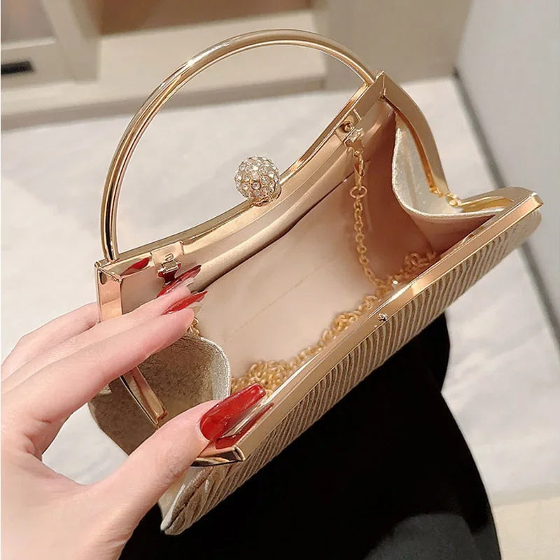 A close-up of a gold pleated glitter evening handbag with a top handle and chain strap being held by a hand.