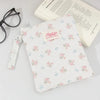 A white floral plaid cotton tablet pouch with a pink tag and a drawstring is shown next to eyeglasses and a book.