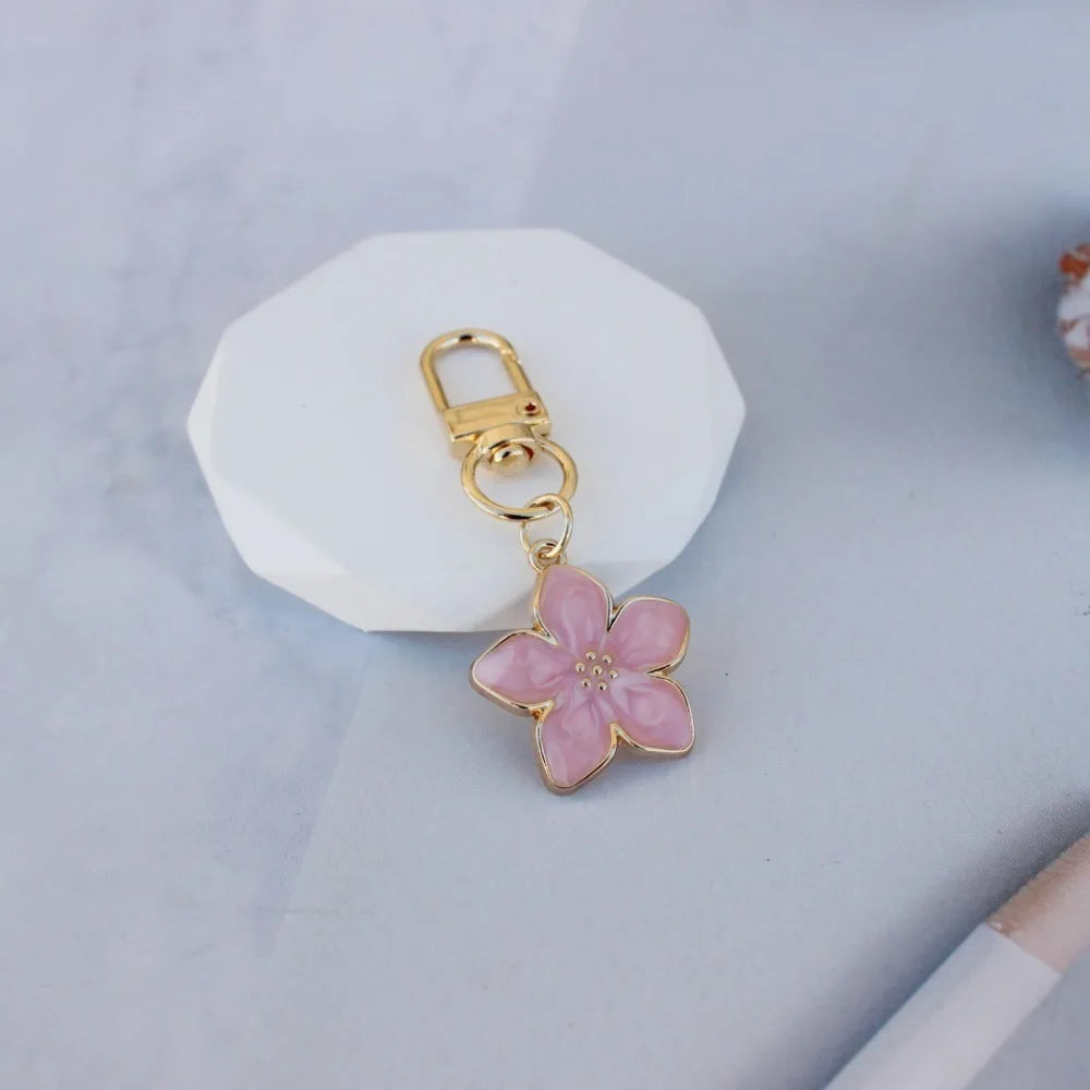 A gold-colored keychain featuring a pink resin flower attached to a split ring.