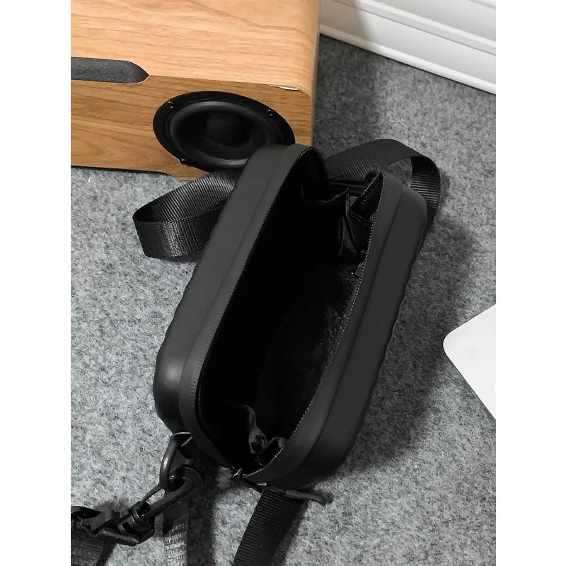 A black PU leather shoulder bag with a strap is shown next to a wooden box and a speaker.