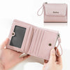 A pink faux leather mini wallet with a zipper and pendant is held in a hand.