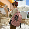A woman wearing a light yellow sweater and brown skirt holds a pink corduroy bow print backpack outdoors.