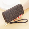 A brown patterned PU leather zippered wallet with a gold-toned strap is shown resting on a light surface.